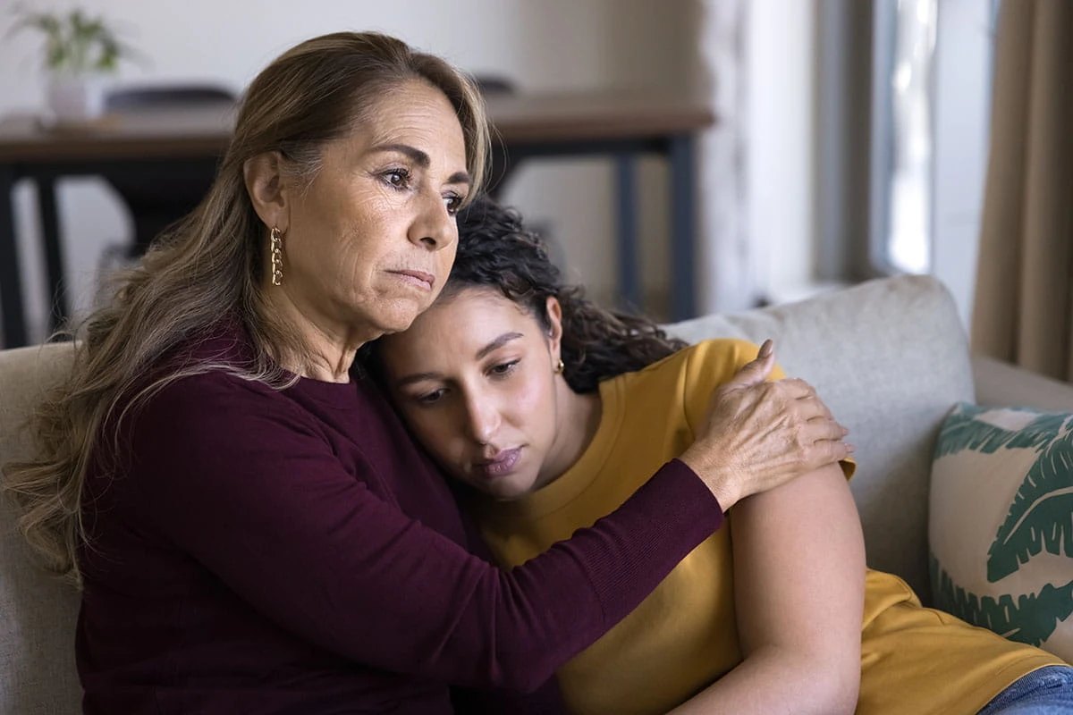 Mãe e filha abraçadas no sofá, em um momento de acolhimento